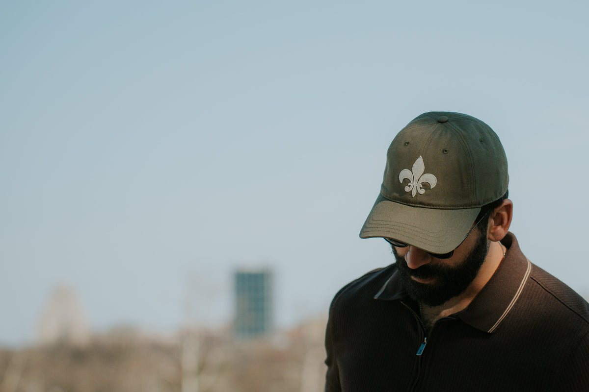 Man wearing a cap with a logo, standing outdoors with a blurred background