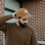 Man wearing a brown cap and sweater against a brick wall.