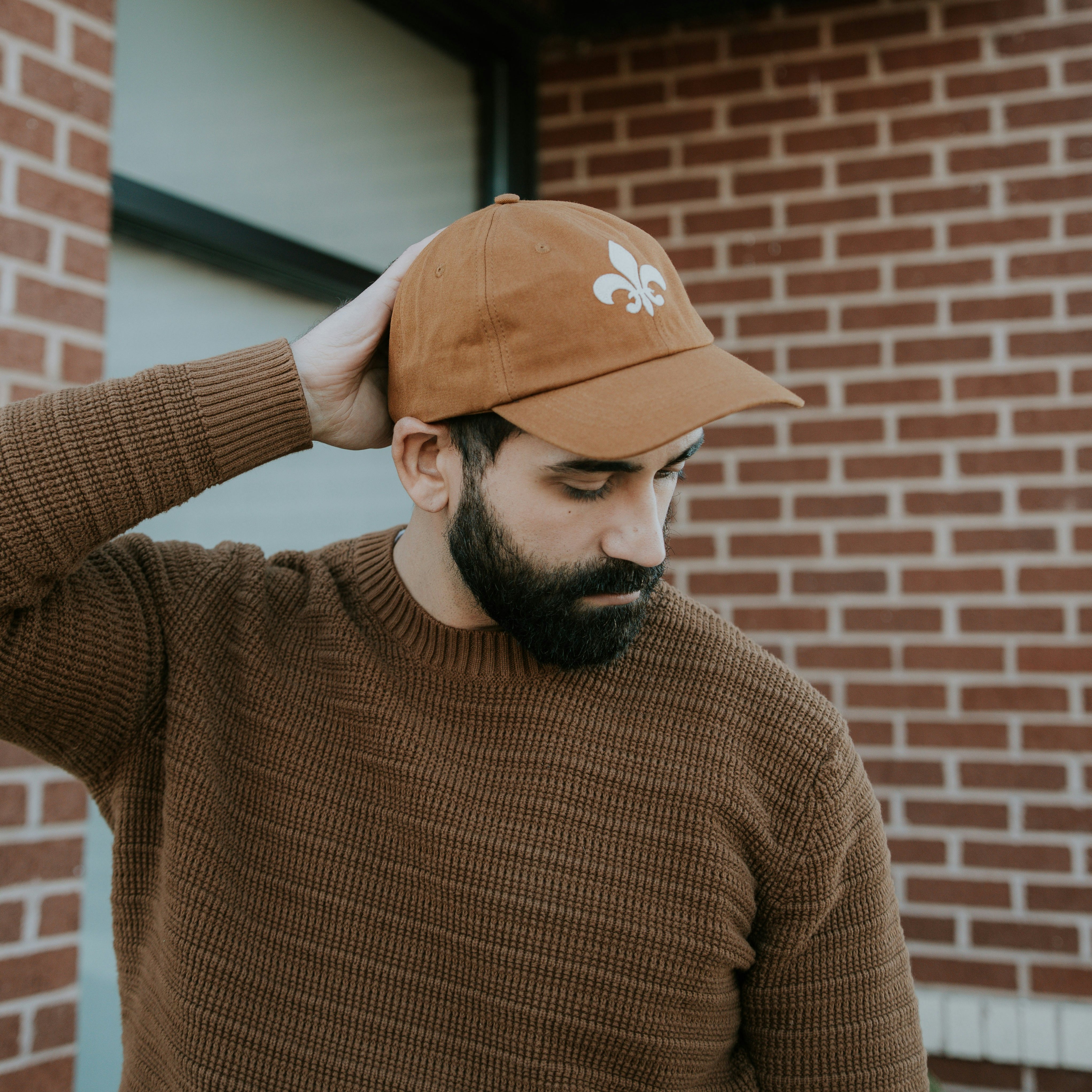 Man wearing the camel organic cotton fleur-de-lis felt patch hat by JON BLANCO against a brick wall in St. Louis