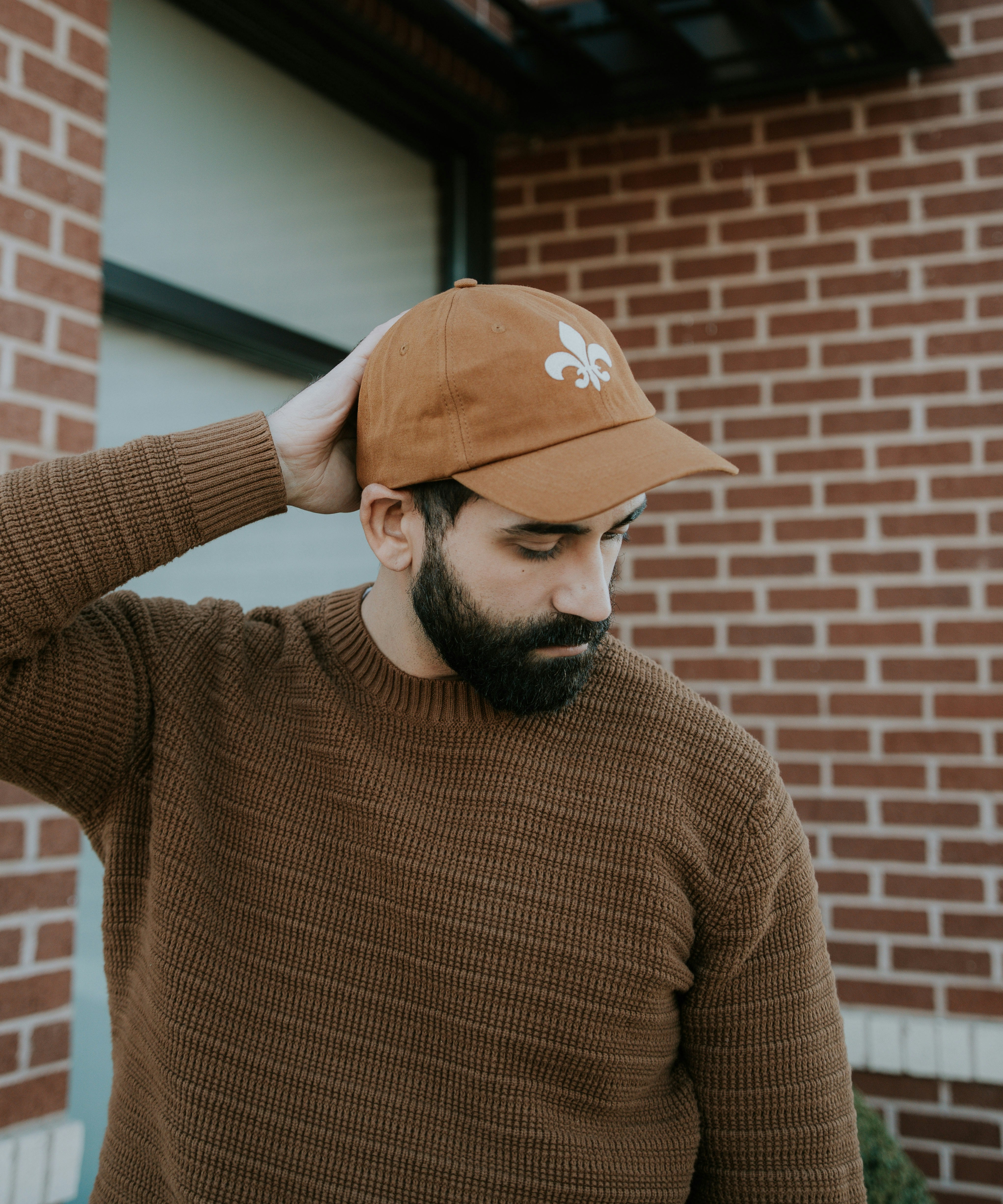 Man wearing the camel organic cotton fleur-de-lis felt patch hat by JON BLANCO against a brick wall in St. Louis