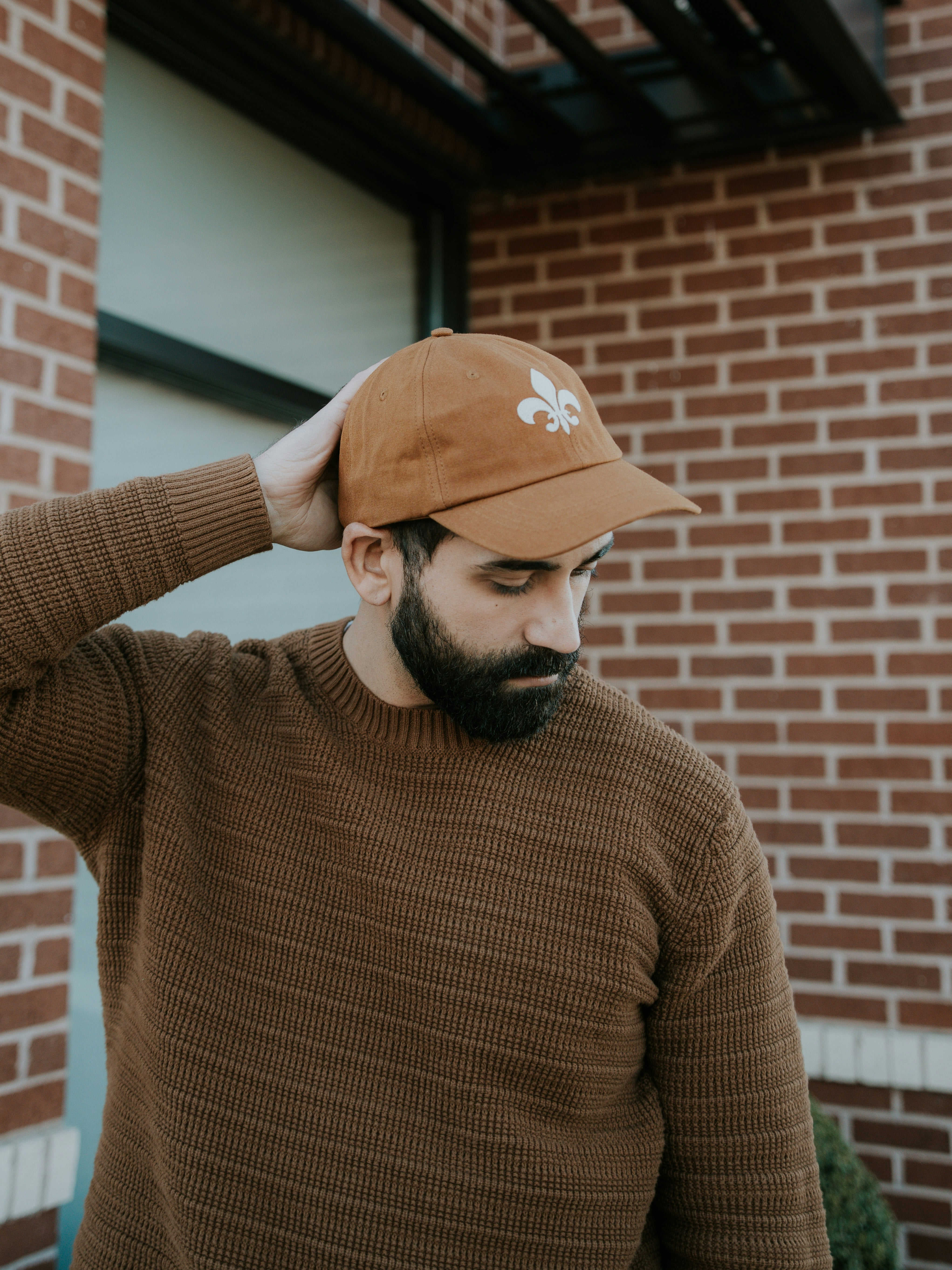 Man wearing a brown cap and sweater against a brick wall.